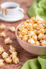 Popcorn with caramel in ceramic bowl on brown concrete background. Side view, selective focus.