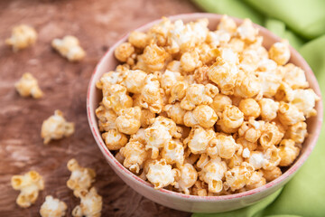 Popcorn with caramel in ceramic bowl on brown concrete background. Side view, selective focus.