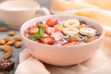 Chocolate cornflakes with milk, strawberry and almonds in ceramic bowl on gray concrete background. Side view, selective focus.