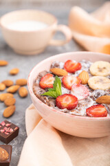 Chocolate cornflakes with milk, strawberry and almonds in ceramic bowl on gray concrete background. Side view, selective focus.