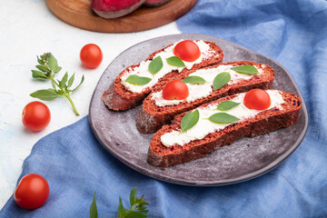 Red beet bread sandwiches with cream cheese and tomatoes on white concrete background. Side view.