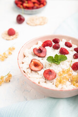 Rice flakes porridge with milk and strawberry in ceramic bowl on white concrete background. Side view, selective focus.