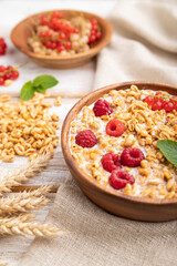 Wheat flakes porridge with milk, raspberry and currant in wooden bowl on white wooden background. Side view, selective focus.