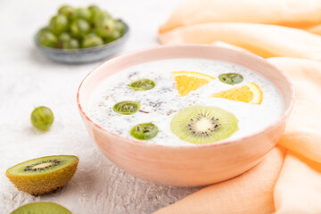 Yogurt with kiwi, gooseberry, chia in ceramic bowl on gray concrete background. Side view, selective focus.