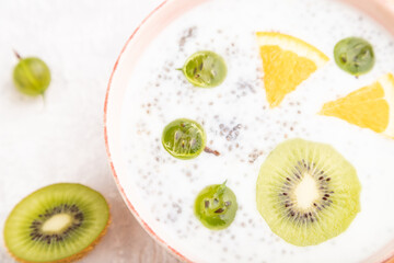 Fototapeta na wymiar Yogurt with kiwi, gooseberry, chia in ceramic bowl on gray concrete background. Top view, selective focus.