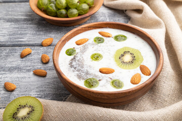 Yogurt with kiwi, gooseberry, chia and almonds in wooden bowl on gray wooden background. Side view, close up.