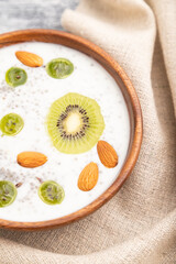 Yogurt with kiwi, gooseberry, chia and almonds in wooden bowl on gray wooden background. Top view, close up, selective focus.