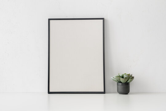Black poster frame and succulent plant on white wall background. Minimalist mockup..