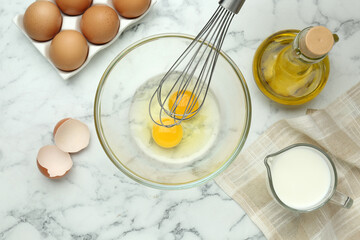 Fototapeta na wymiar Whisking eggs in bowl near other ingredients on white marble table, flat lay