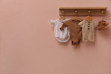 Wooden rack with cute baby clothes and shoes on pink wall indoors. Space for text