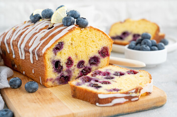 Lemon blueberry cake with lemon icing and fresh berries on top on the board on a gray concrete...