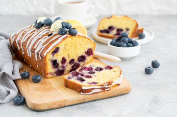Lemon blueberry cake with lemon icing and fresh berries on top on the board on a gray concrete...