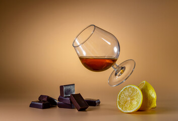 A glass of cognac and pieces of chocolate on a bright background. Levitation.