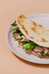 Italian Piadina with roast beef, sun-dried tomatoes, wild garlic, pesto, mozzarella and bechamel sauce. Beige background.