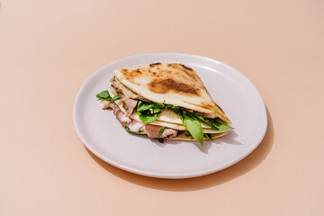 Italian Piadina with roast beef, sun-dried tomatoes, wild garlic, pesto, mozzarella and bechamel sauce. Beige background.