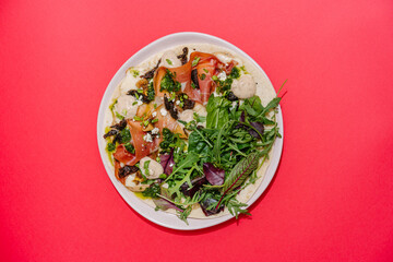 Italian Piadina with prosciutto, sun-dried tomatoes, greens mix, pesto, bechamel and mozzarella. Red background. top view