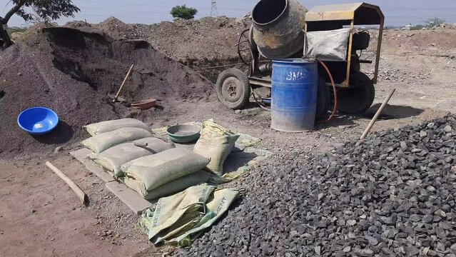 Footage of concrete mixer machine, sand, cement bags, and crusher stone kept at the construction site for new building construction - Construction materials