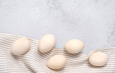Five eggs on a striped linen napkin or towel on light gray textured background. Easter card in pastel colors with copy space. Wooden egg for creativity, coloring.