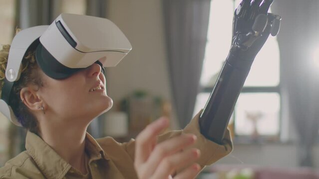 Girl with prosthetic arm touching something in air and looking around while playing video game with VR headset at home