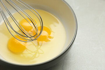 Whisking eggs in bowl on light grey table, closeup