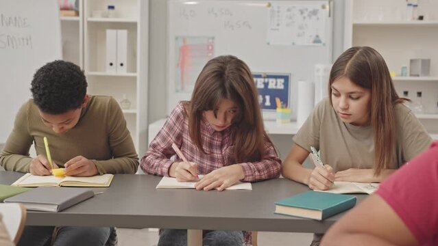 Waist up slowmo of multiethnic elementary school girls trying to cheat at test when teacher getting them caught