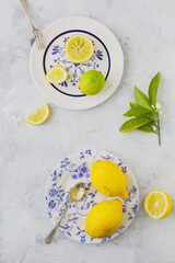 Vintage plates with yellow and green citrus next to an old knife and spoon on a white background and an orange tree branch with orange blossom