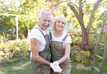 Portrait of joyful senior couple of gardeners in love, wearing aprons and dancing in their garden