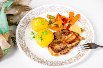 Roasted pork steak, boiled potato and baked vegetable on white plate.