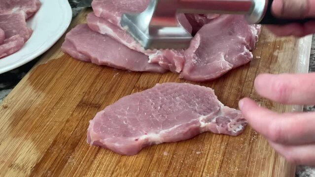 Tenderizing pork cut with meat mallet tool - using meat pounder meat tenderizer to prepare slabs of pork and seasoning with salt for pork schnitzels recipe at home in kitchen slo-mo slow motion