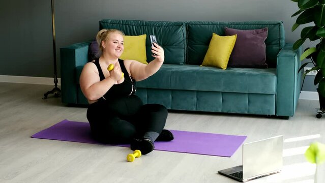 A fat obese woman takes pictures of herself on her phone posing for the camera during a sports home workout. A lazy woman shares photos of her fitness classes, where she did everything just for show. 