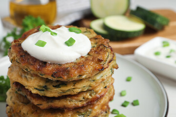 Delicious zucchini pancakes with sour cream served on table, closeup