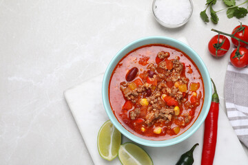 Bowl with tasty chili con carne and ingredients on white table, flat lay. Space for text
