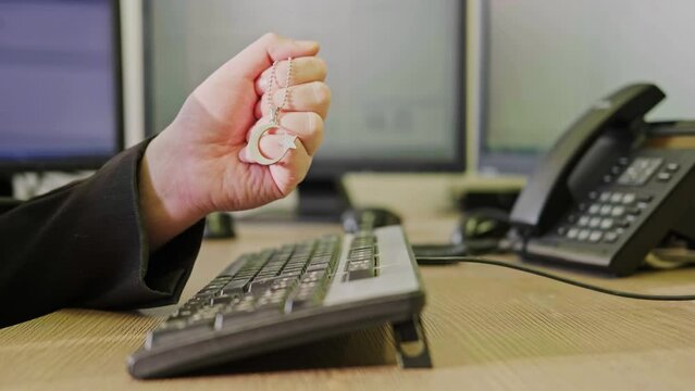 A businessman man with a religious Muslim symbol in his hands is working on a computer keyboard at an office desk, close-up