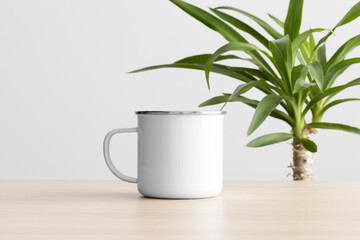 Enamel mug mockup on the wooden table with a yucca plant.