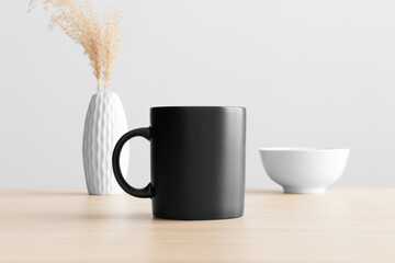 Black mug mockup with a dry flower decoration on the wooden table.