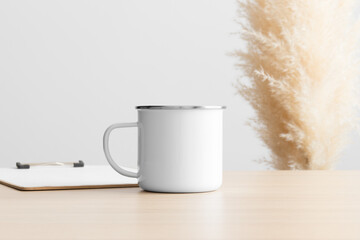 Enamel mug mockup with a clipboard on the wooden table with a pampas decoration.
