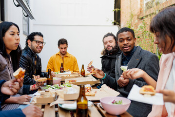 Group of multiracial friends celebrating with lunch at a restaurant. focus on an African man, holding a piece of pizza and discussing veganism with his friend who is holding a piece of lettuce.
