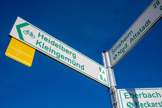 Signpost for bicycle tours with distance information which guides to "Heidelberg", "Kleingemuend", "Sinsheim" and "Eberbach" in Baden-Wuerttemberg, Germany against blue sky
