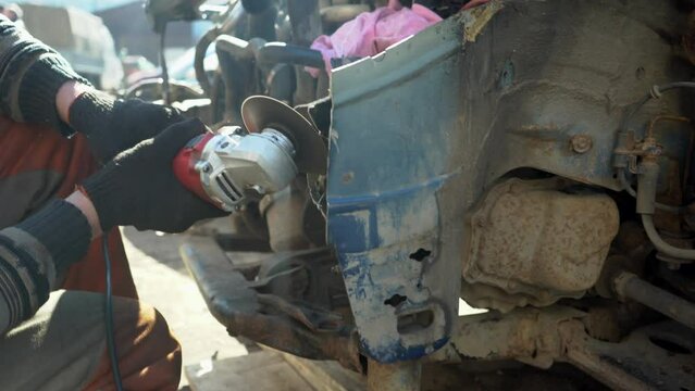 A locksmith cuts out a metal part of a car body with a tool. Dismantling a transport for auto parts in the garage. During operation, many bright yellow sparks fly to the sides.