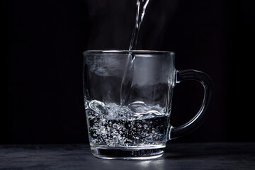 Boiling water is poured into a glass on a black background. Hot drinking water