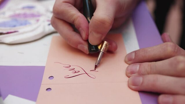 Process of calligraphy handwriting with an ink fountain pen feather, calligrapher practicing writing on a postcard paper using pen brush and sign pen with inkwell on master-class lesson, hands view