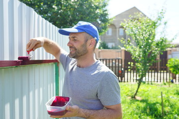 senior man working in garden. Worker painting fence. Summer outdoor activity. Development 