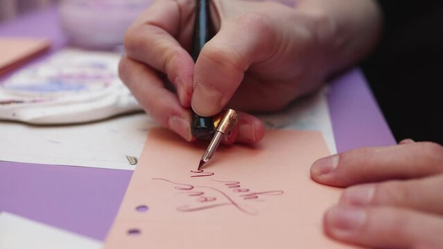 Process of calligraphy handwriting with an ink fountain pen feather, calligrapher practicing writing on a postcard paper using pen brush and sign pen with inkwell on master-class lesson, hands view