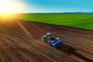 Farmer with tractor seeding crops at field - obrazy, fototapety, plakaty