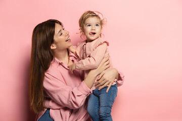 Play. Portrait of young woman and little girl, mother and daughter isolated on pink studio...