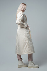 attractive woman in white coat and trousers looking at camera on grey background