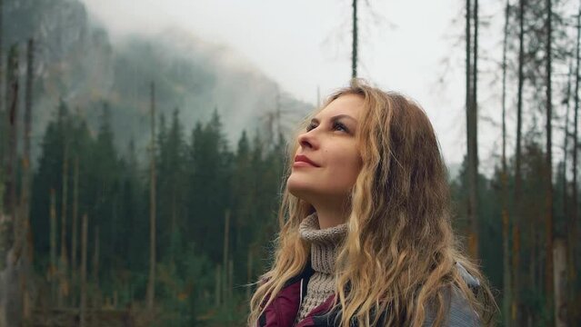 Video with noise. Young happy woman tourist walks in Polish Carpathian mountains Zakopane. pine green trees. Hiker girl puts raises face to sky under drops of rain, wet skin eyes closed. Enjoy nature 