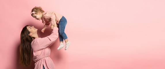Fototapeta Play. Portrait of young woman and little girl, mother and daughter isolated on pink studio background. Mother's Day celebration. Concept of family, childhood, motherhood obraz