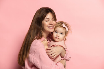 Huggins. Portrait of young woman and little girl, mother and daughter isolated on pink studio background. Mother's Day celebration. Concept of family, childhood, motherhood