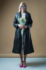 Blond young smiling happy woman in coat and dress with bouquet isolated on beige background studio
